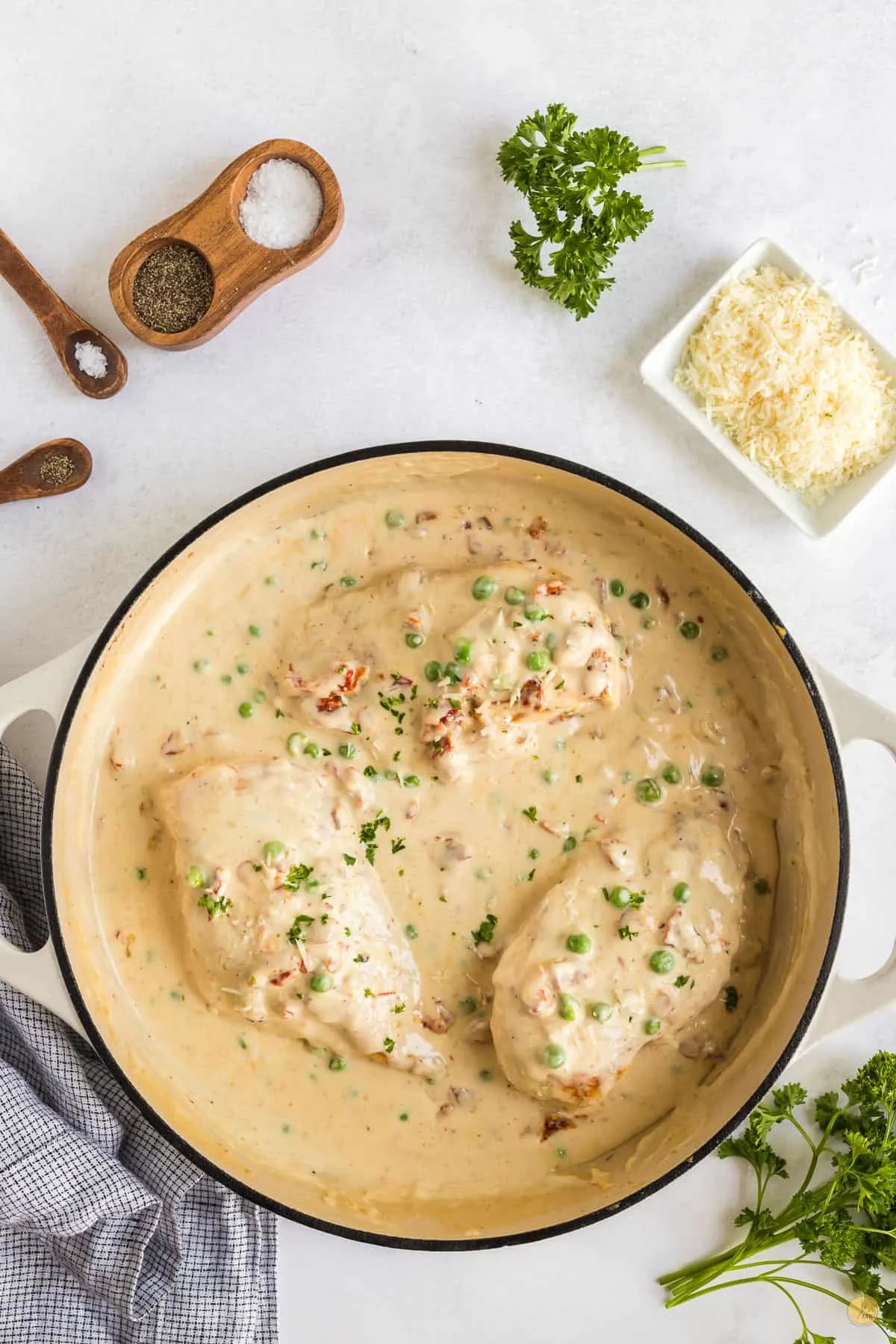 white pan with three pieces of chicken and peas in a cream sauce