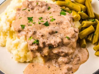a white plate filled with mashed potatoes with sausage gravy with green beans on the side.
