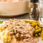 a white plate filled with mashed potatoes with sausage gravy with green beans on the side.