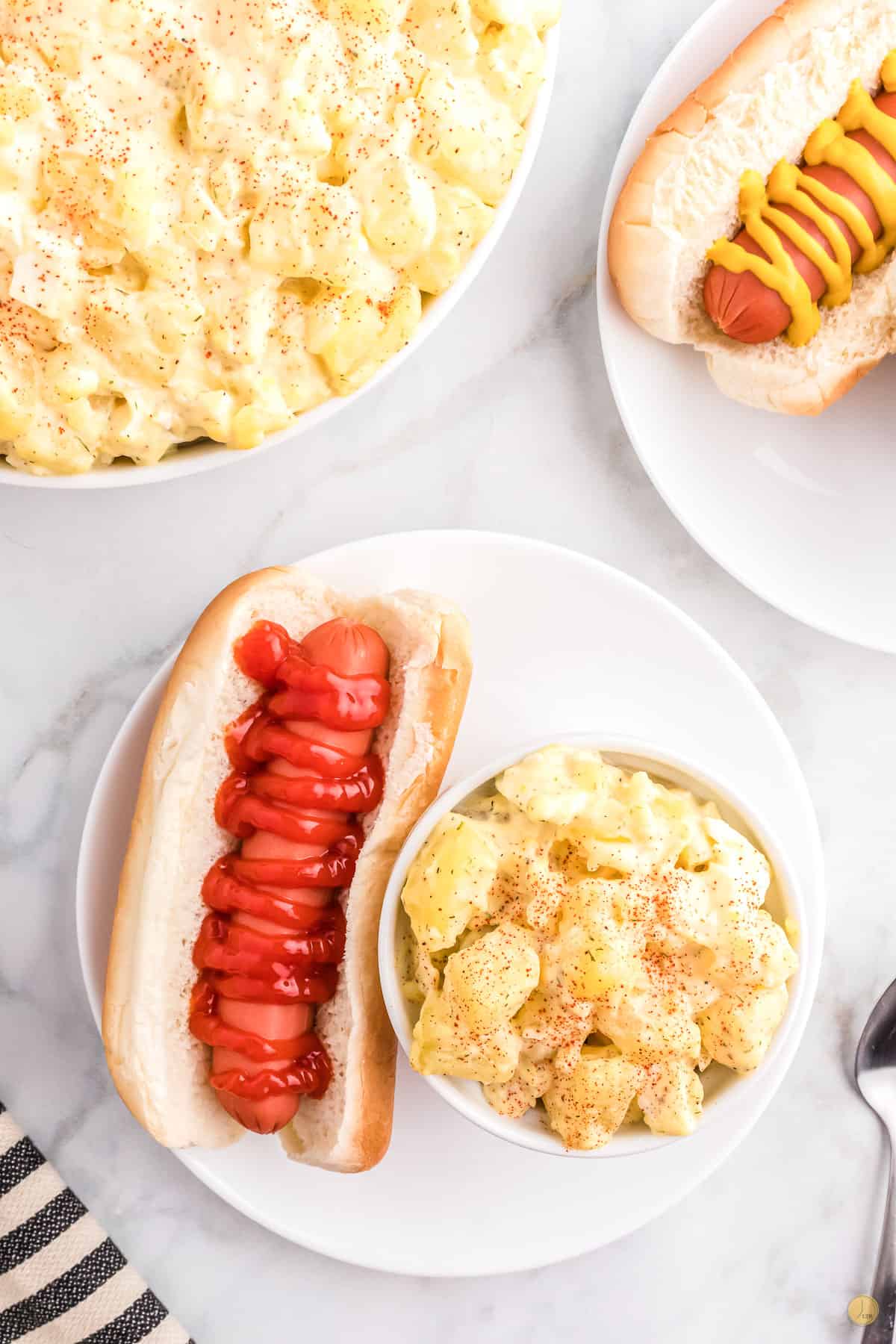 bowl of potato salad on a plate with a hot dog dressed with ketchup
