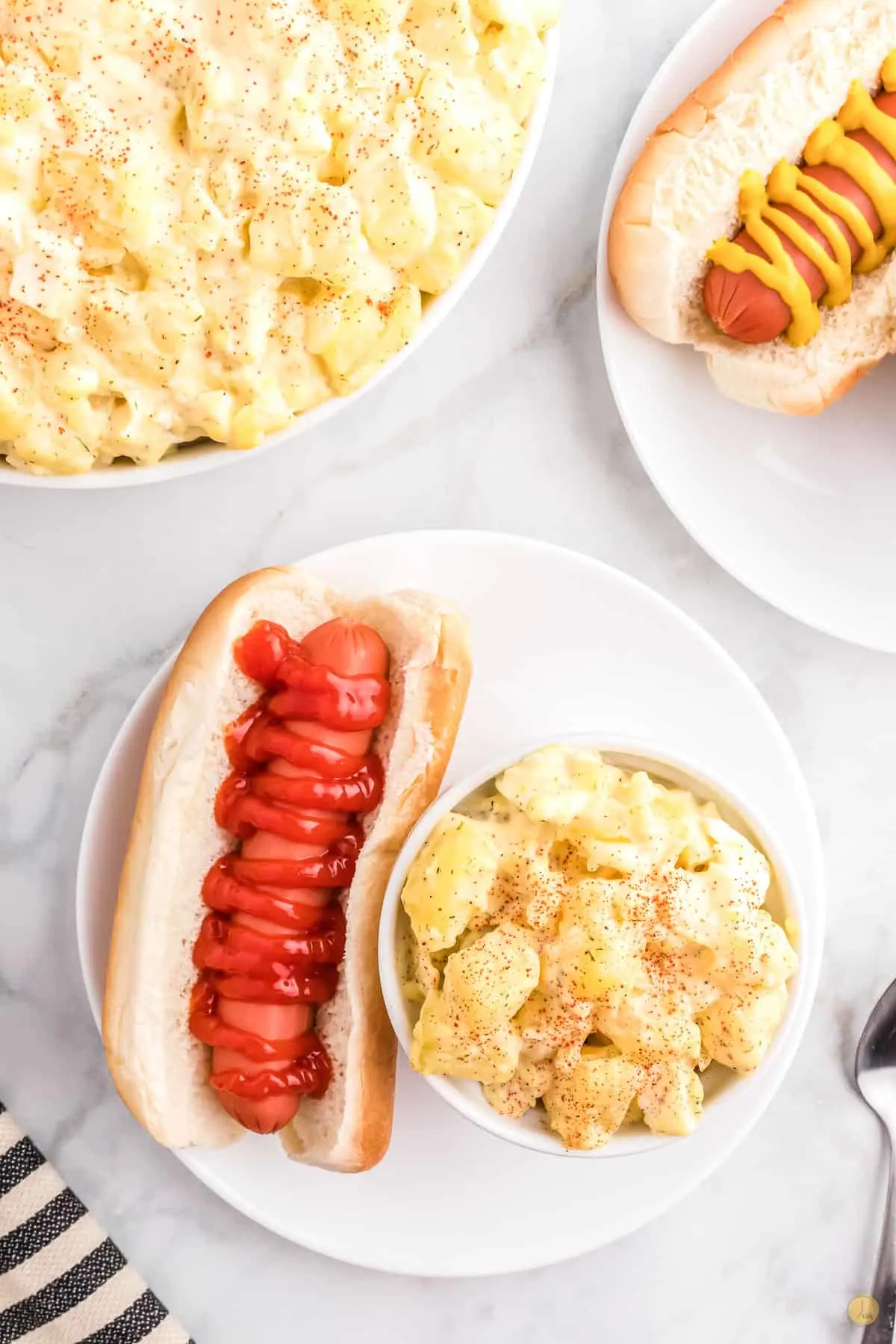 bowl of potato salad on a plate with a hot dog dressed with ketchup