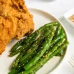 Top view close up of a white round plate with fried chicken on it with spicy green beans on the side