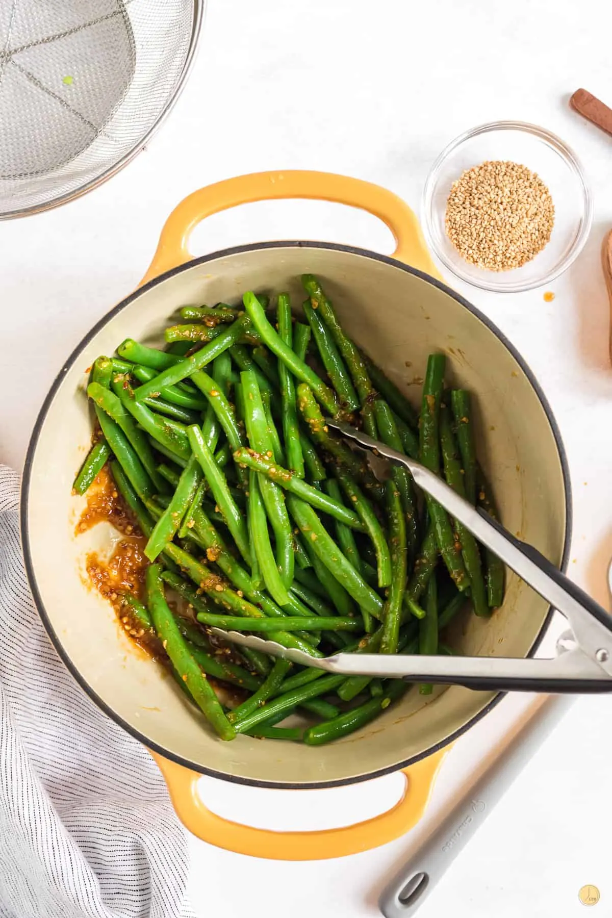 Top view of a dutch oven with green beans being cooked in a brown sesame seed sauce.