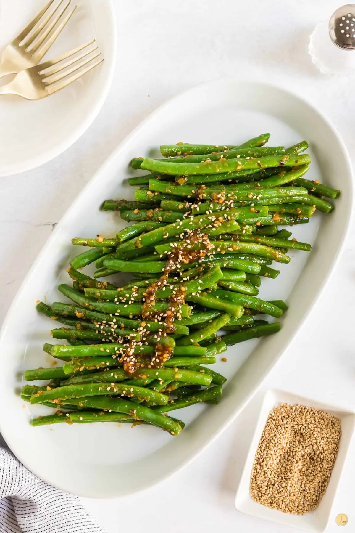 Top view of a white oval plate filled with spicy green beans in a brown sesame seed sauce. 