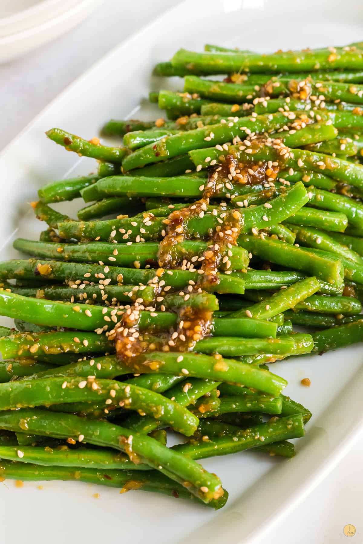 Close up of a white plate filled with spicy green beans with a brown sesame seed sauce on top. 