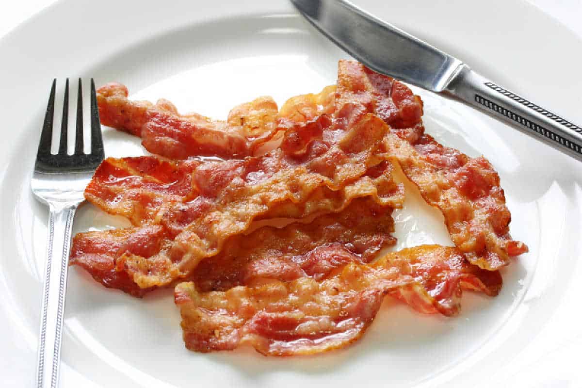 Just cooked bacon on a white plate with a knife and fork