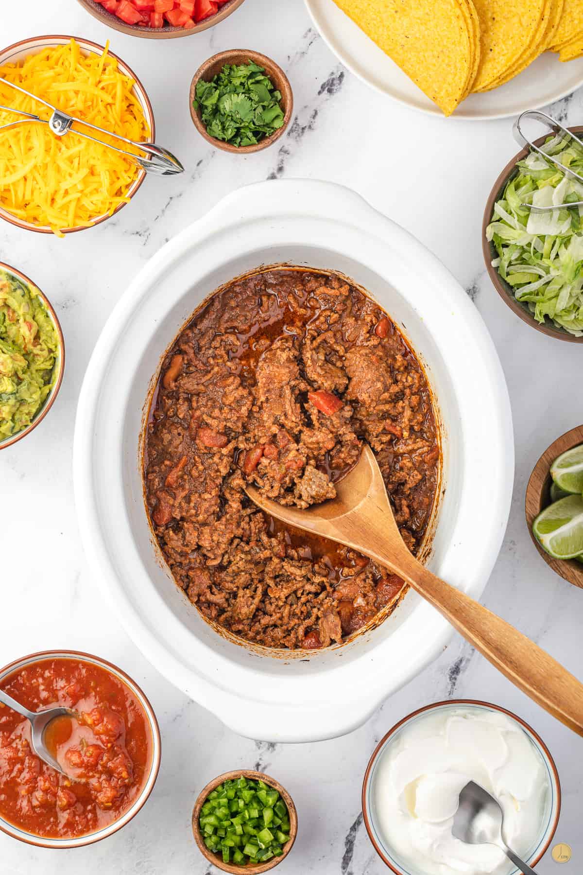 white slow cooker with ground beef and salsa with a wood spoon