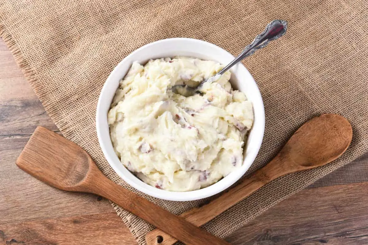 white bowl of mashed potatoes with wood serving utensils
