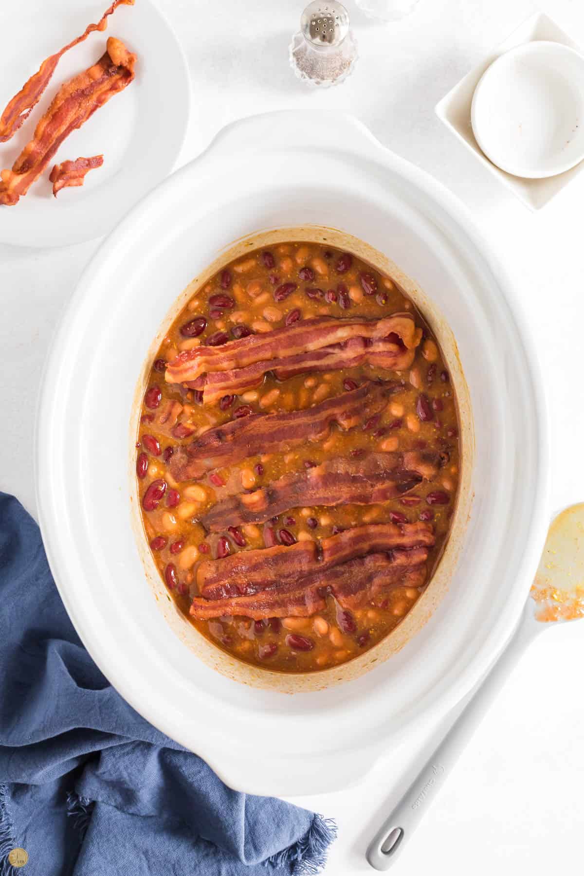 beans with strips of bacon in a white slow cooker