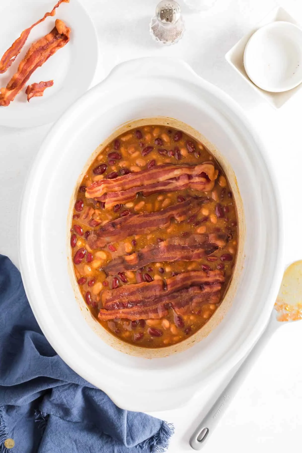 beans with strips of bacon in a white slow cooker