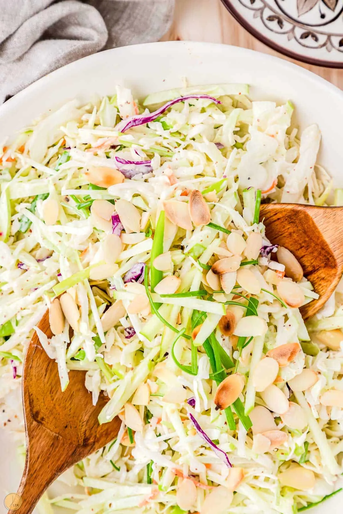 bowl of apple slaw with two spoons and sliced almonds
