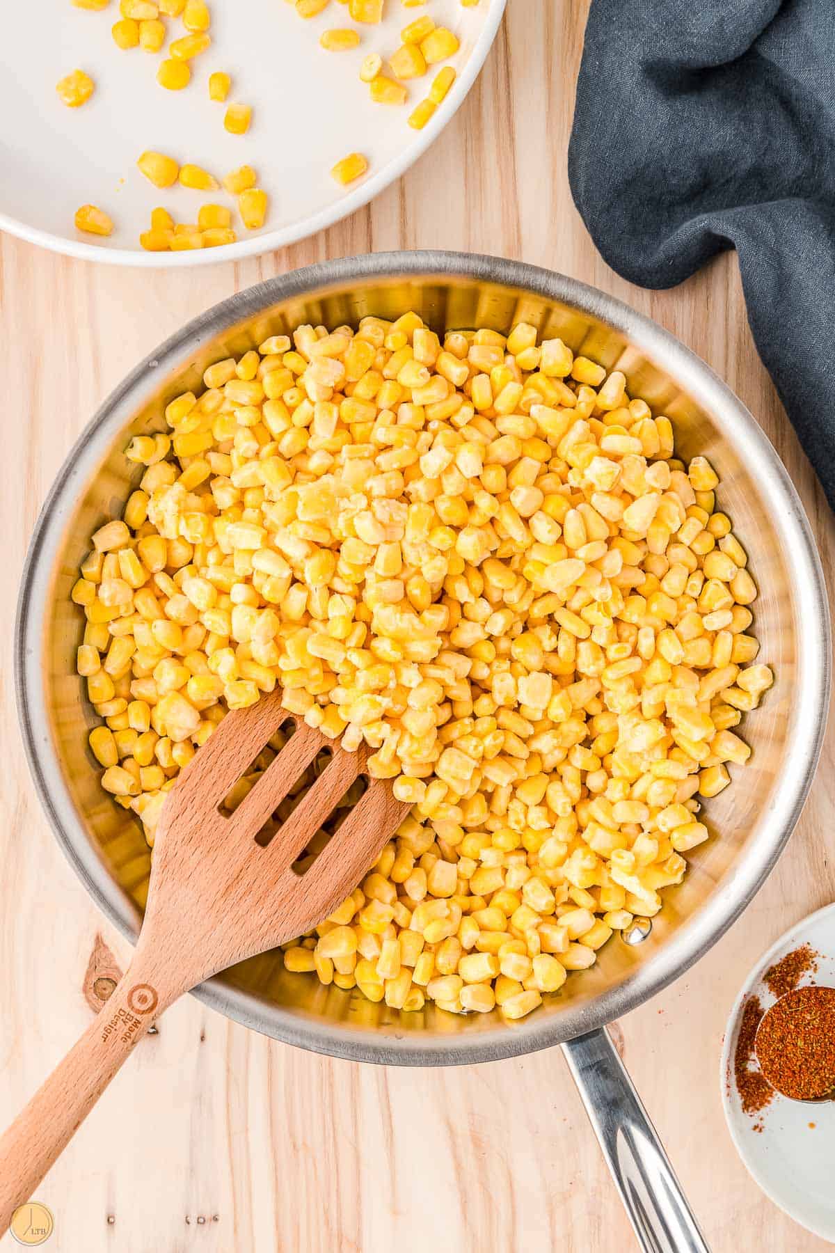 frozen corn kernels in a skillet with a wood spatula
