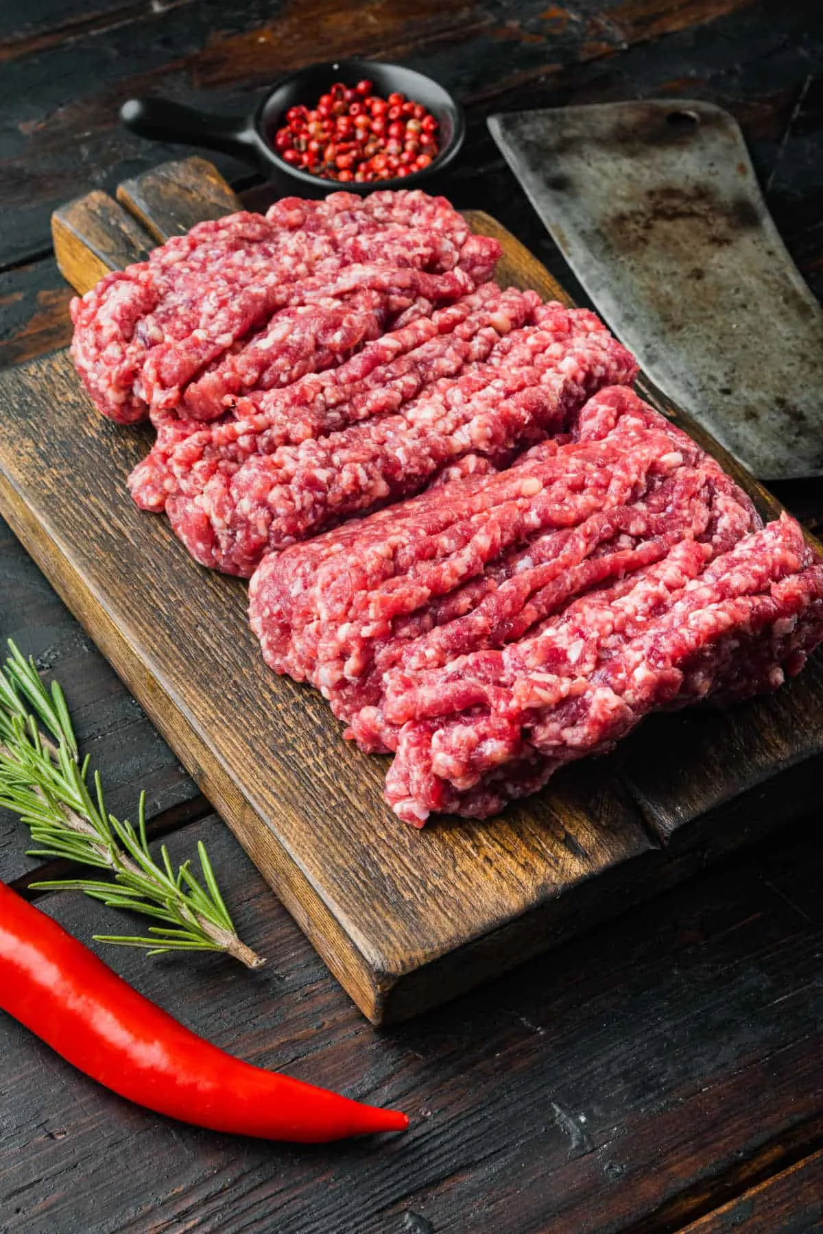 ground beef on a wood surface with peppercorns and a cleaver