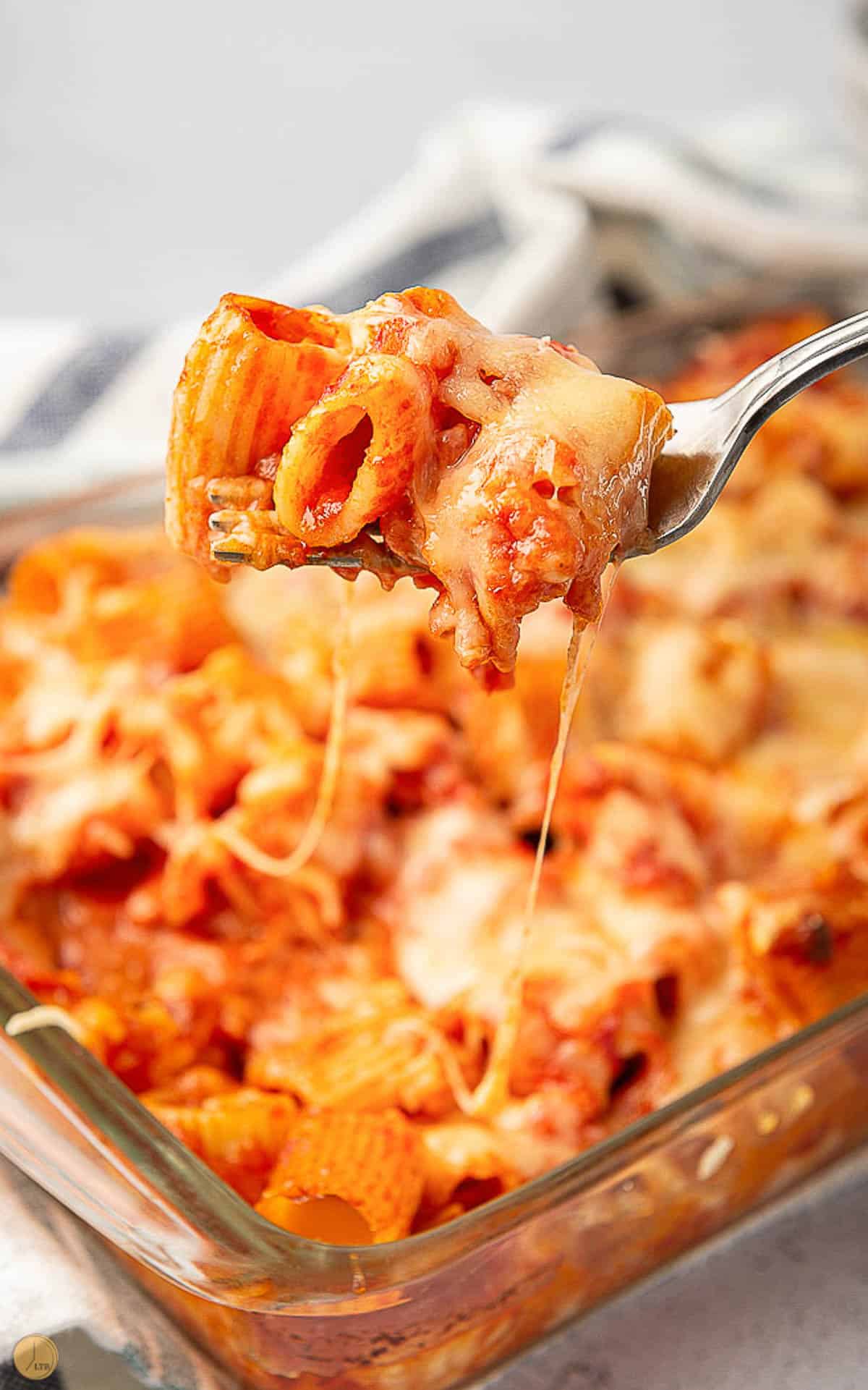 fork with pasta and melted cheese with casserole dish of baked pasta in the background