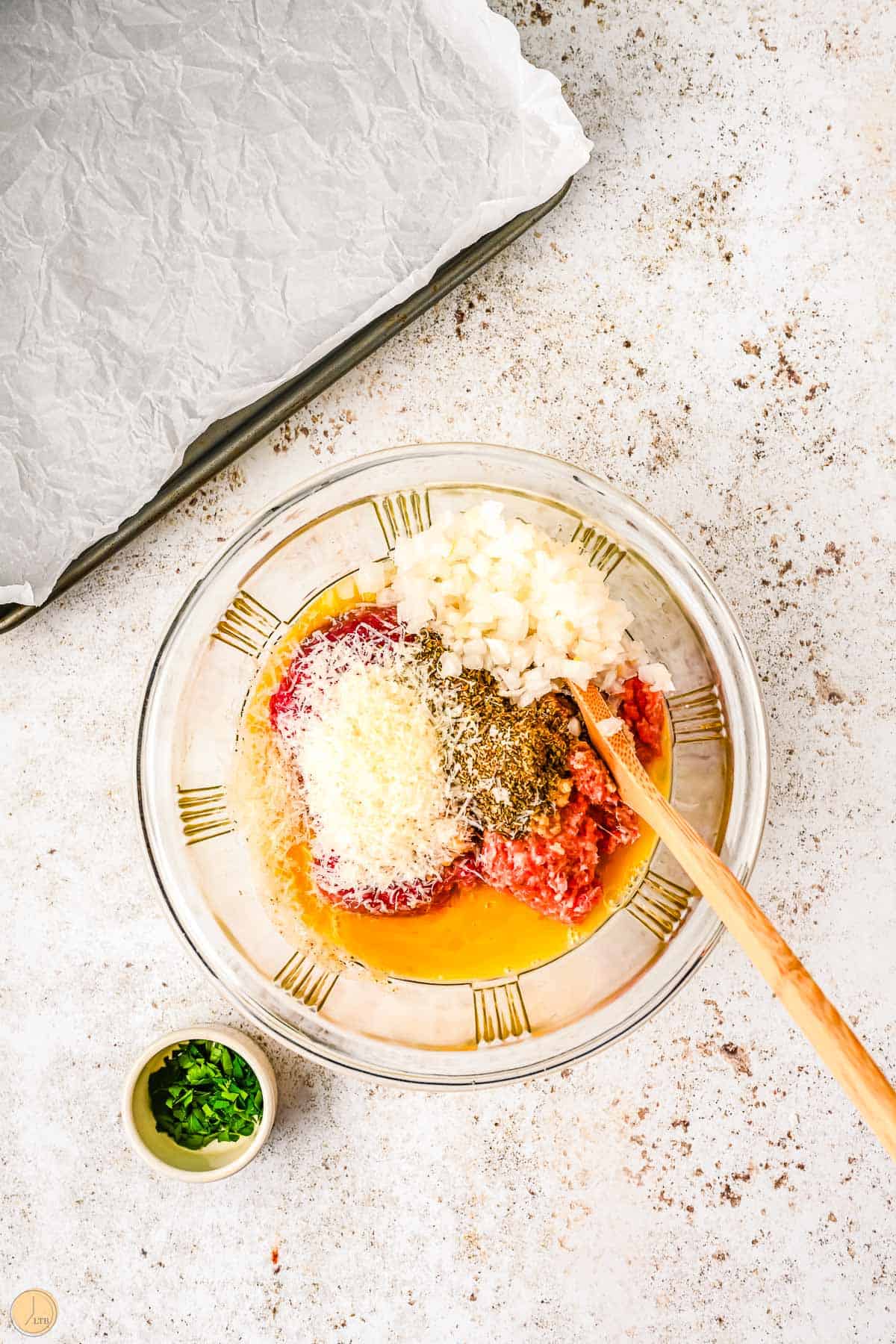 meatball mixture in a clear bowl with a wood spoon