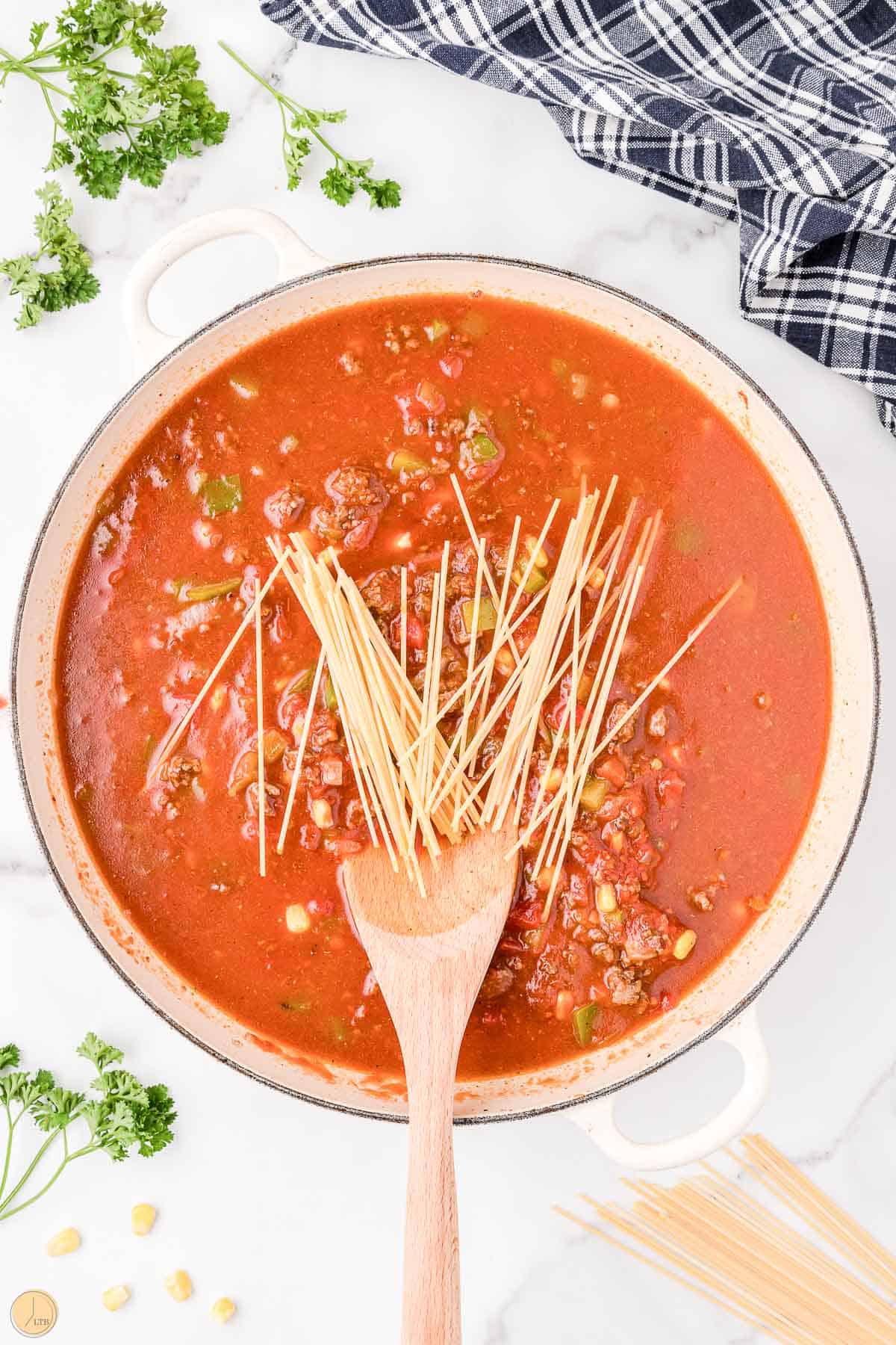 pot with broken pasta noodles and sauce in a pan with a spoon