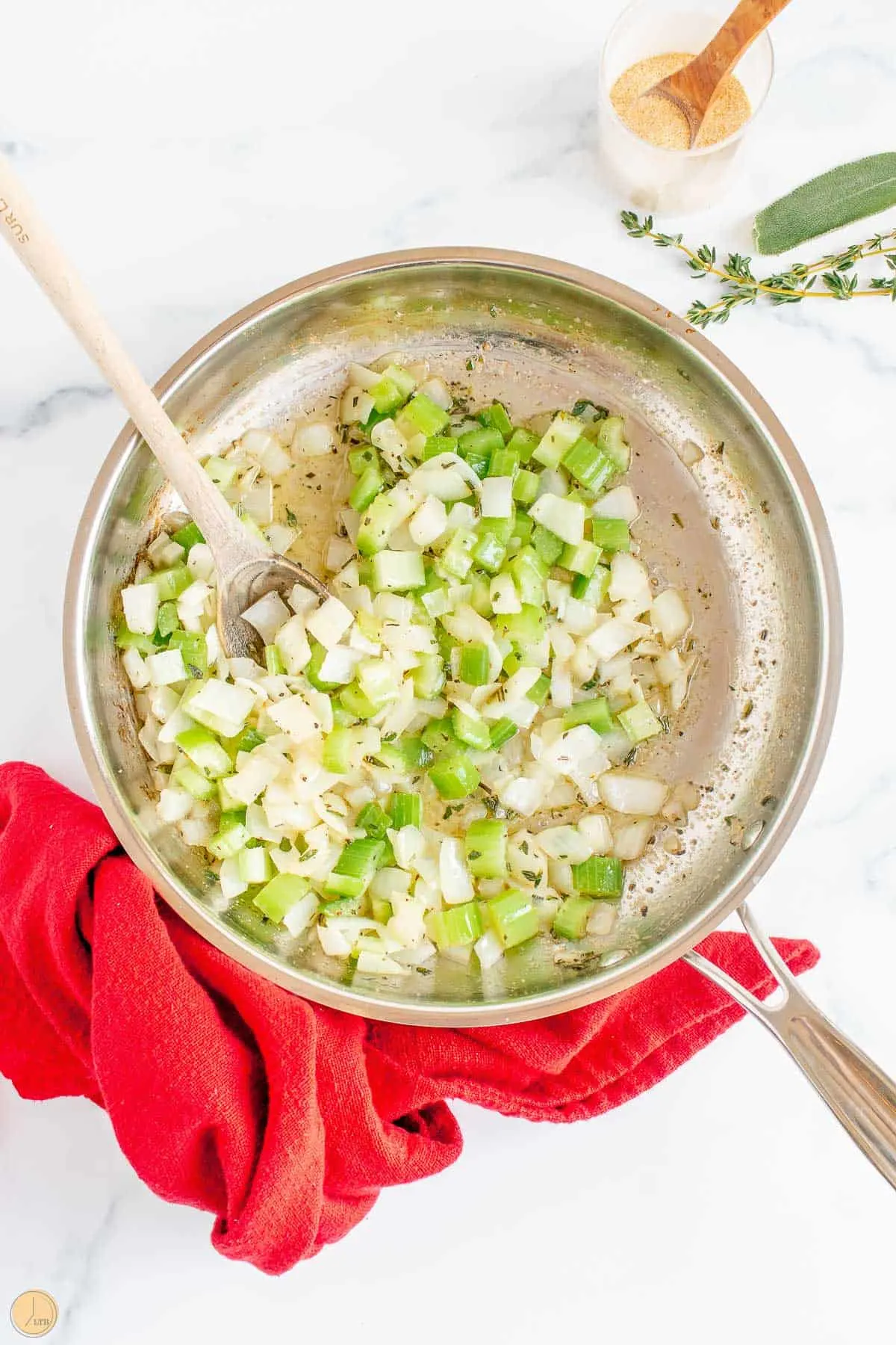 onions and celery cooking in a sauce pan with a red napkin and wood spoon