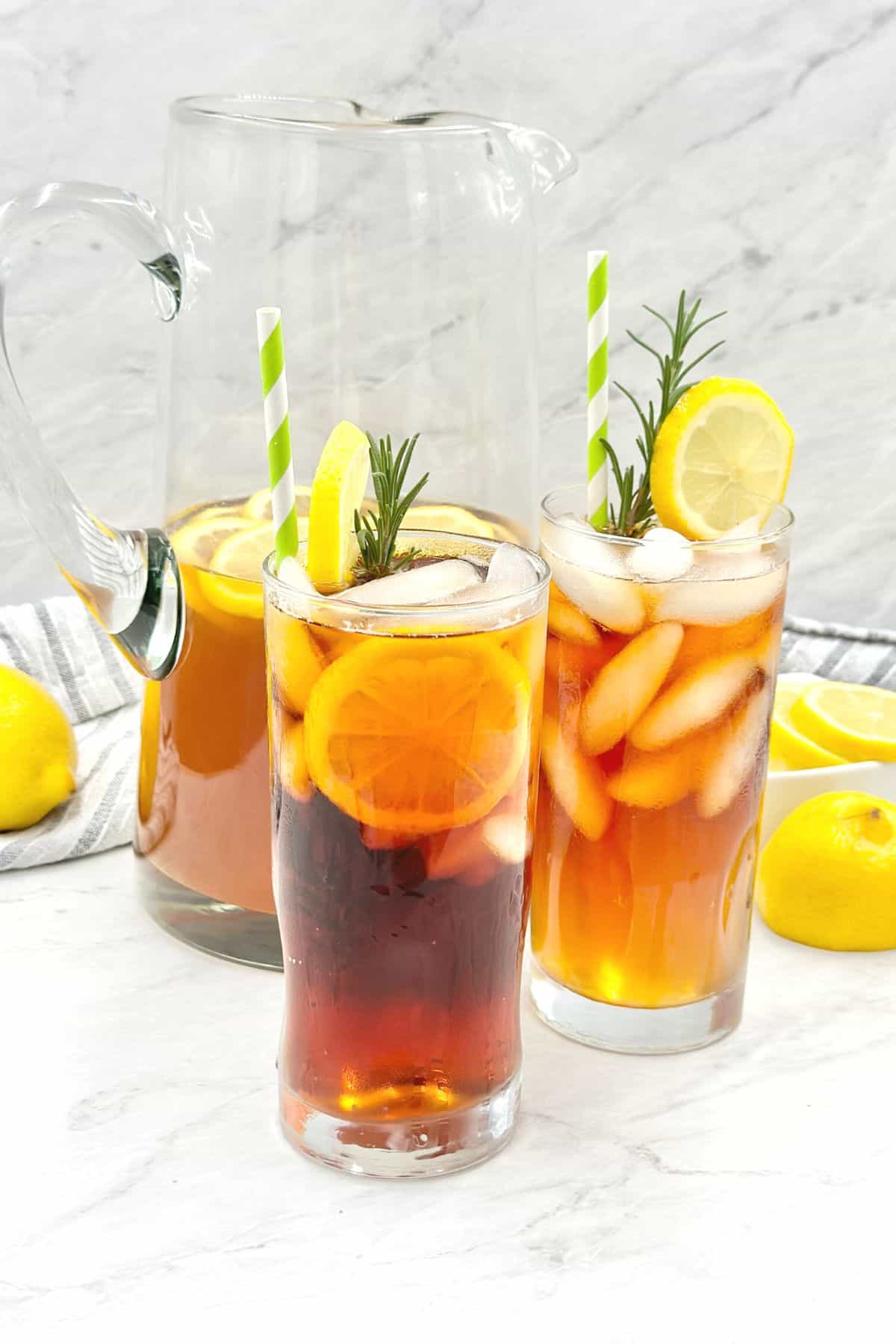 side view of lemon iced tea in glasses with fresh herbs and lemon slices