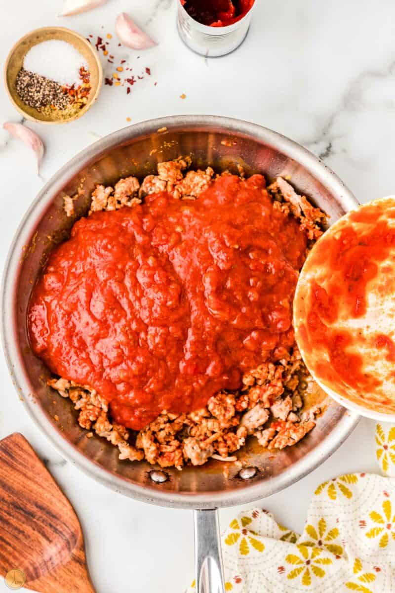 browned ground meat in a skillet with tomato sauce being poured on it