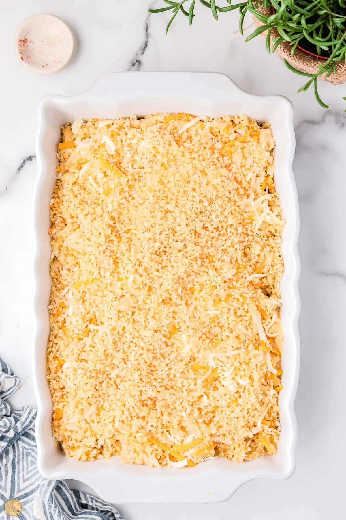 breadcrumbs and shredded cheese on top of casserole in a white dish