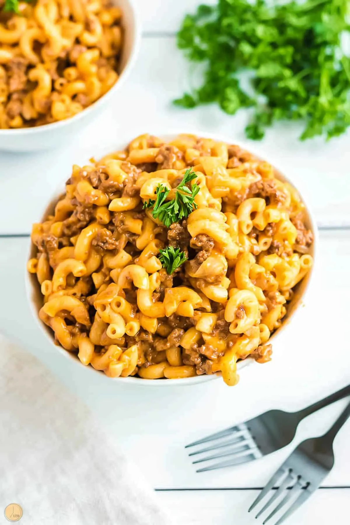 two bowls of homemade hamburger helper on a white board with bunch of parsley
