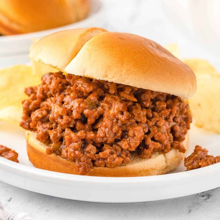 sloppy joes sandwich on a white plate with chips
