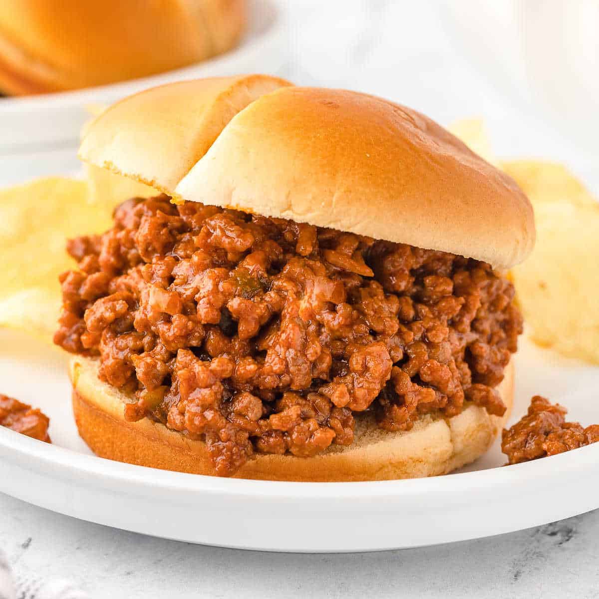 sloppy joes sandwich on a white plate with chips