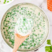 pot of peas with a cream sauce and a wood spatula
