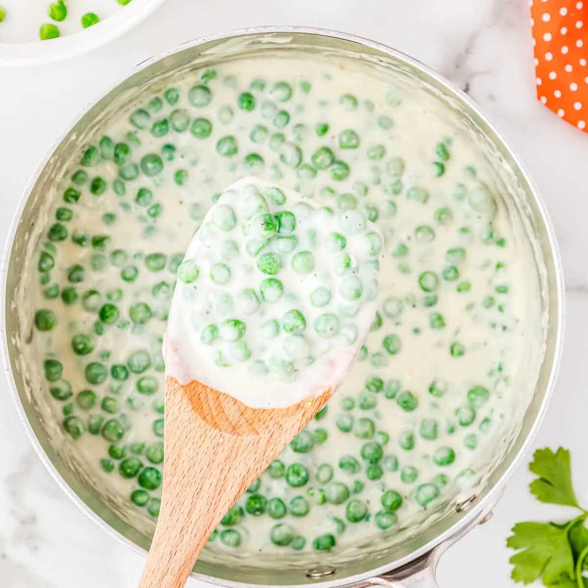 pot of peas with a cream sauce and a wood spatula