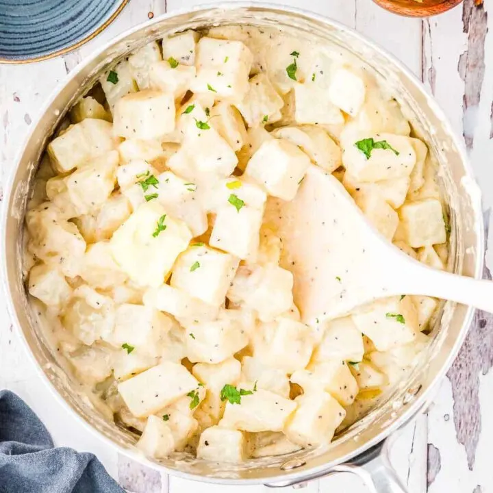 overhead picture of large skillet with creamed potatoes in it and a white spoon