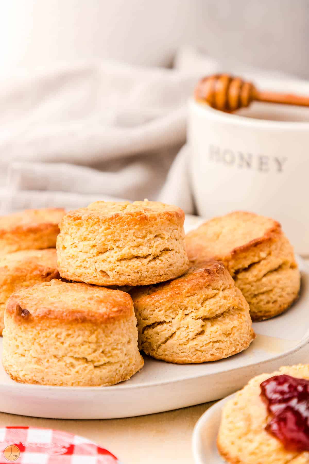 stack of honey biscuits on a white plate with a honey pot in the back