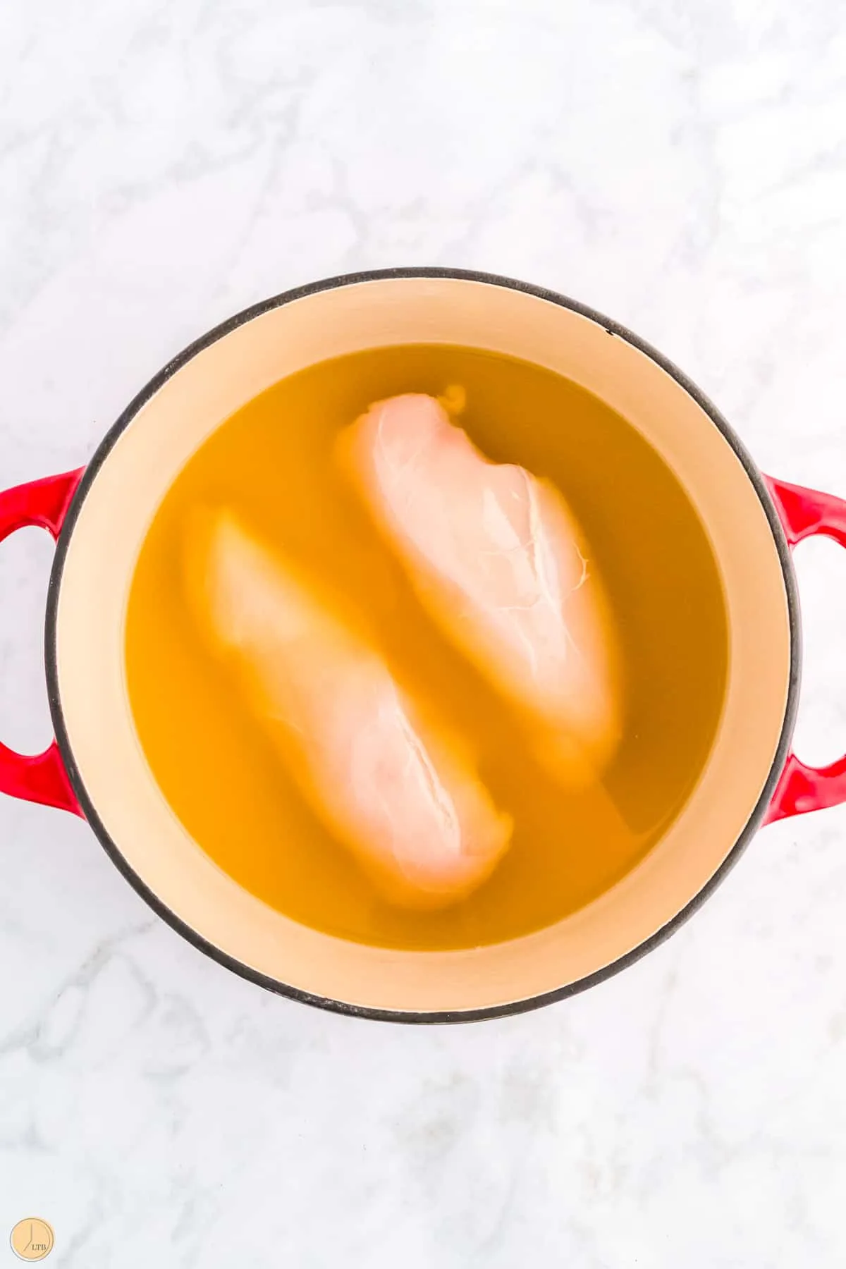 chicken breasts in broth in a red pot