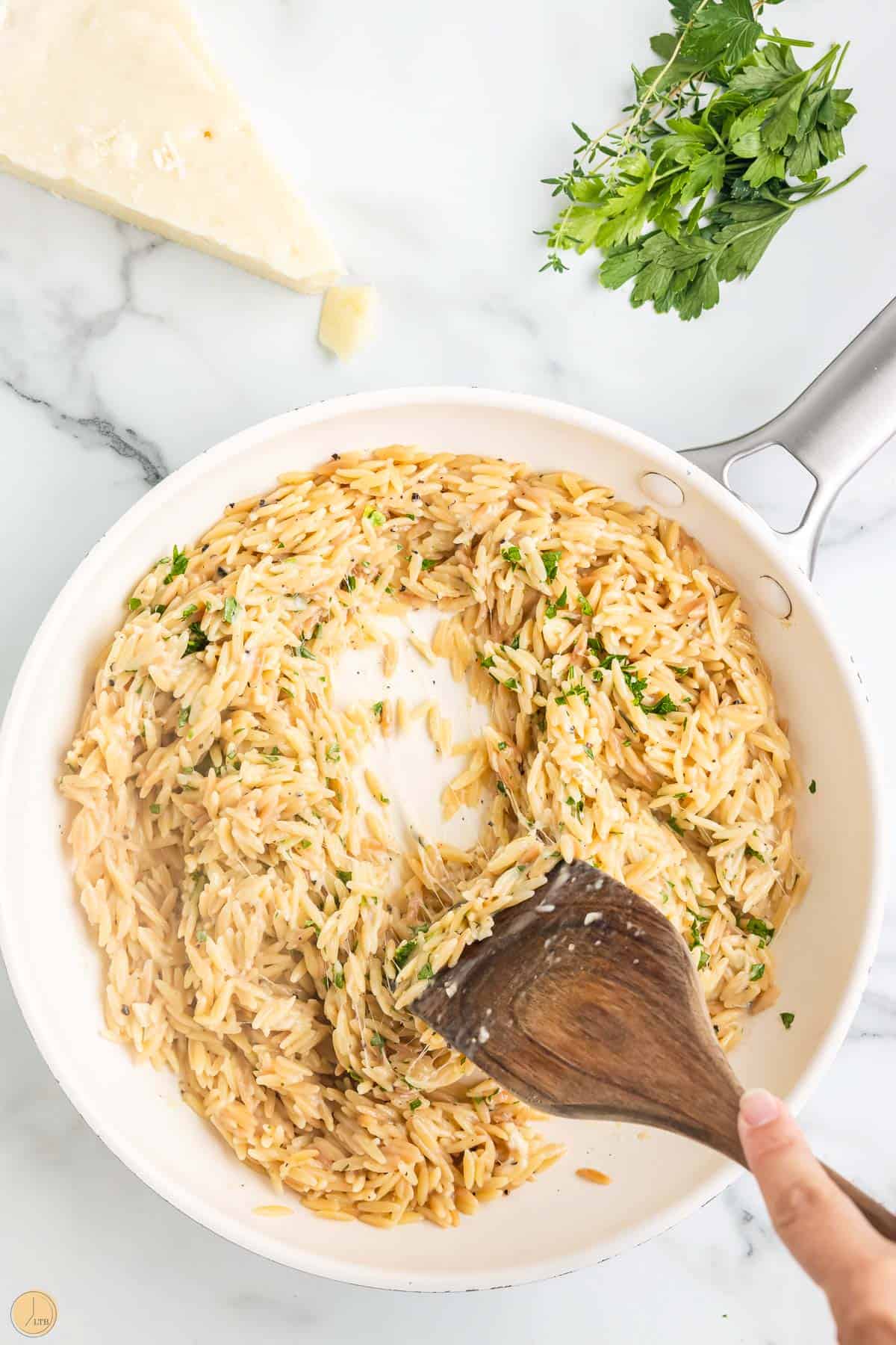 wooden spoon stirring parmesan orzo in a skillet
