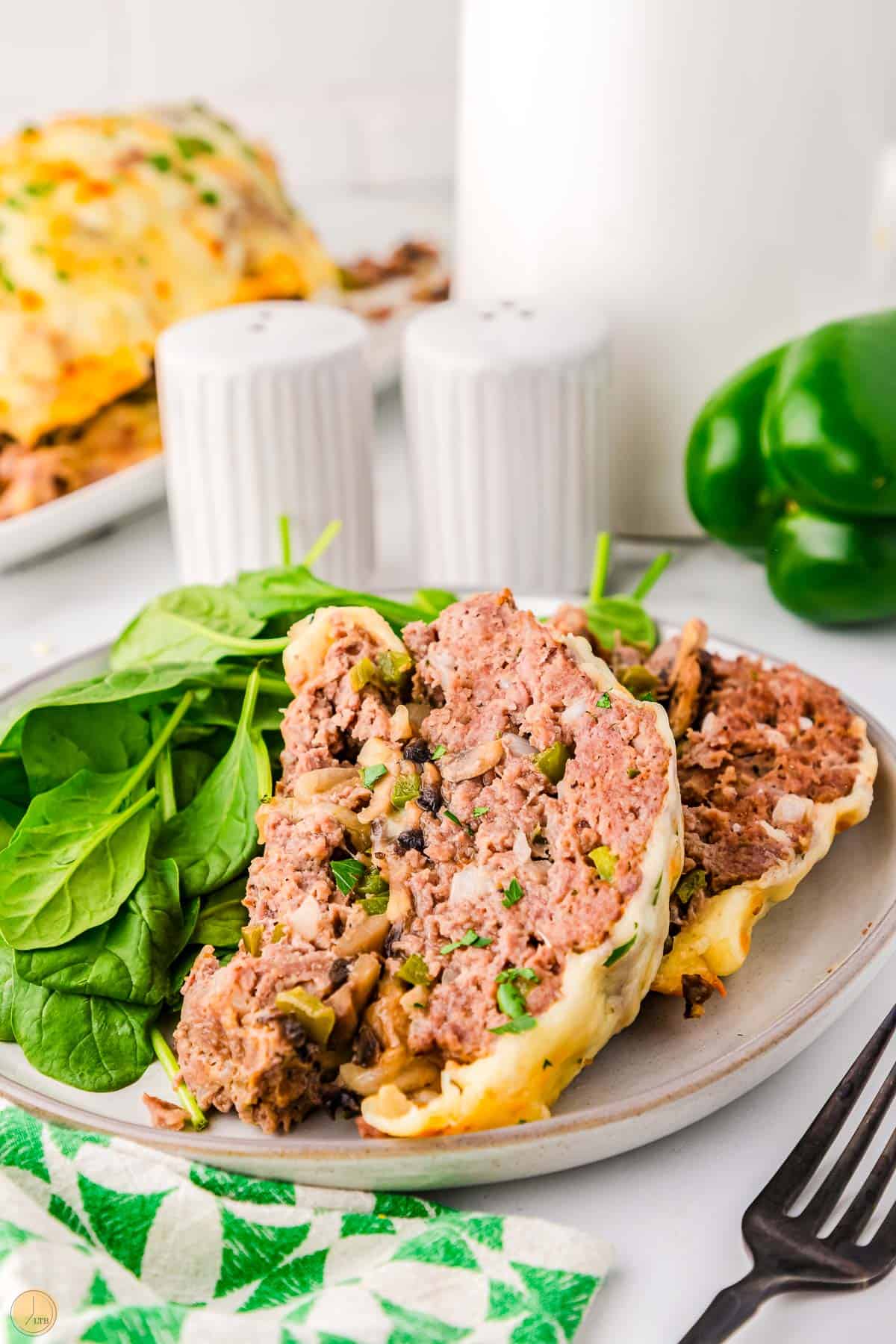 two slices of meatloaf on a plate with fresh spinach