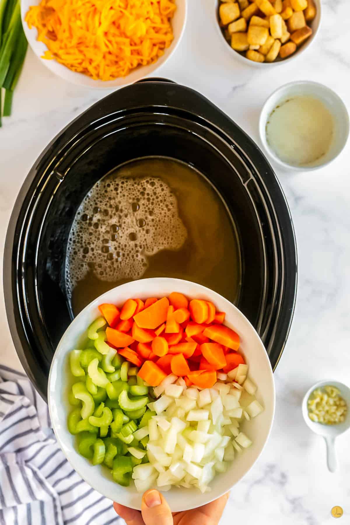 celery, carrots, and onion being poured into a crock pot