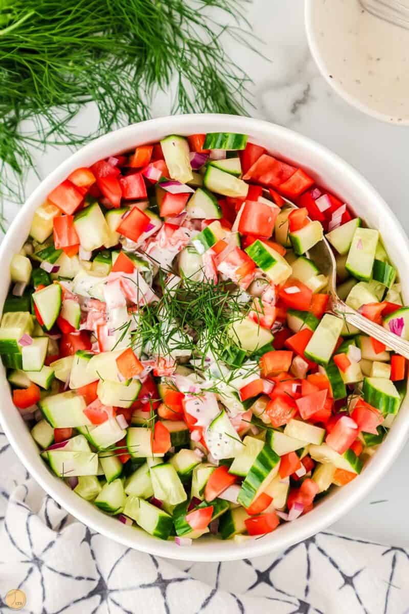 chopped cucumbers and tomatoes with dressing and dill on top