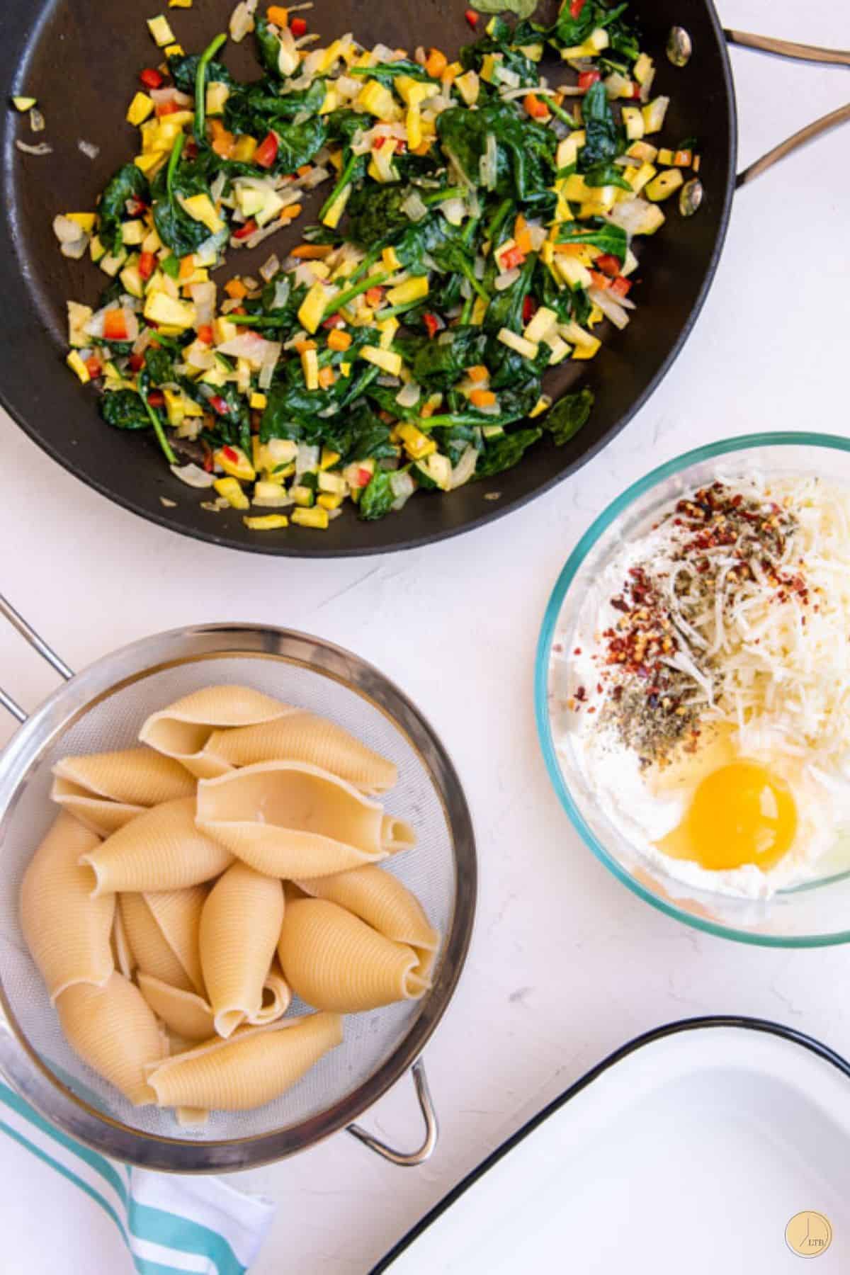 cooked pasta shells, cheese, and cooked veggies in a skillet