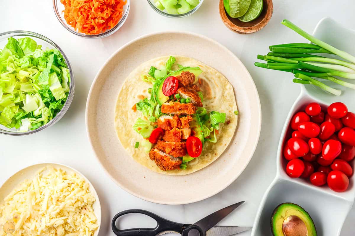 plate with chicken wrap on it surrounded by bowls of toppings.