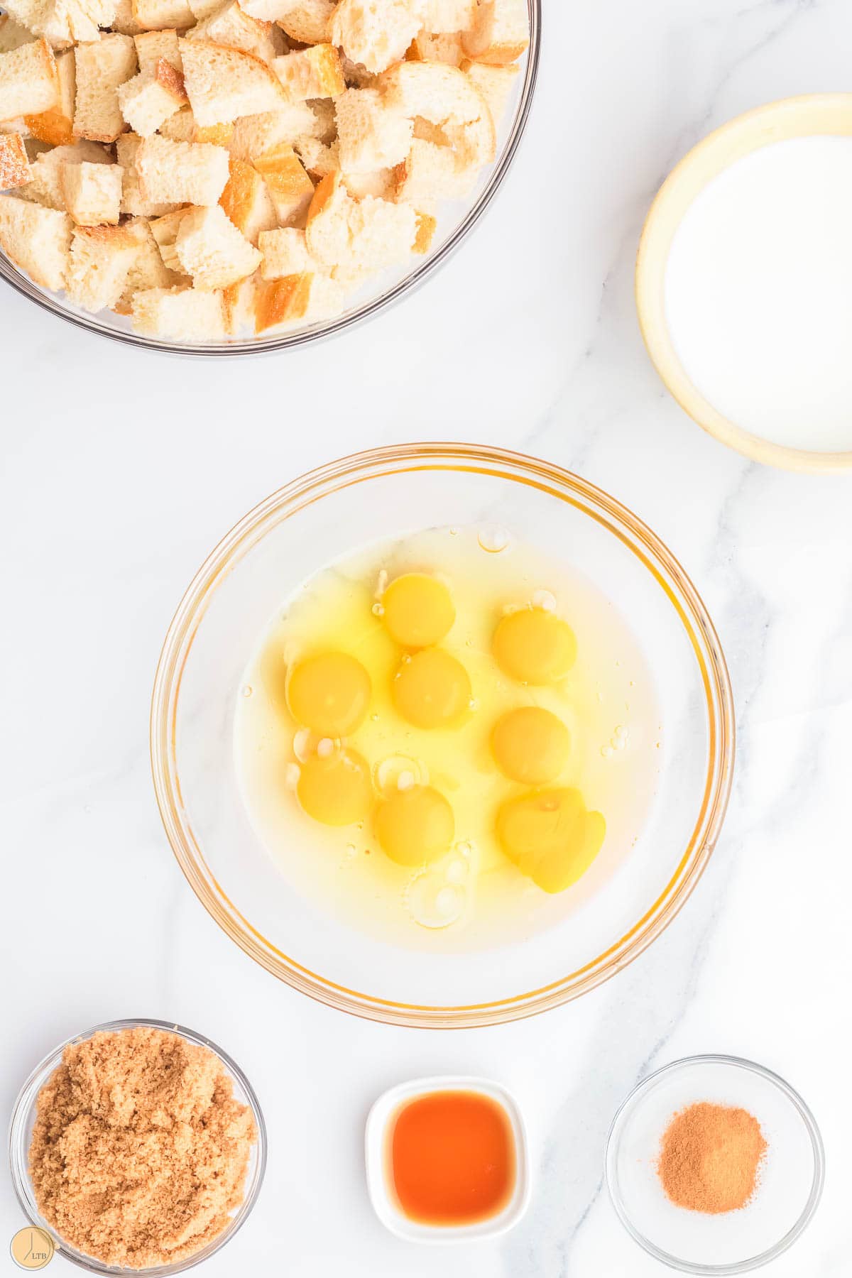 cracked eggs in a mixing bowl with milk and brown sugar around it