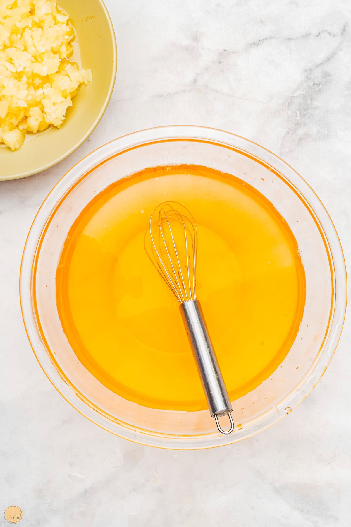 pineapple jello in a clear bowl with a whisk