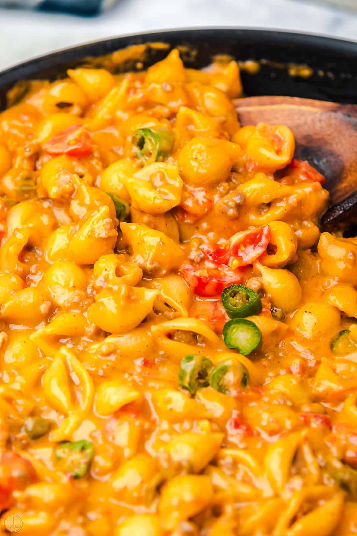 skillet of pasta and cheese sauce with a wooden spoon