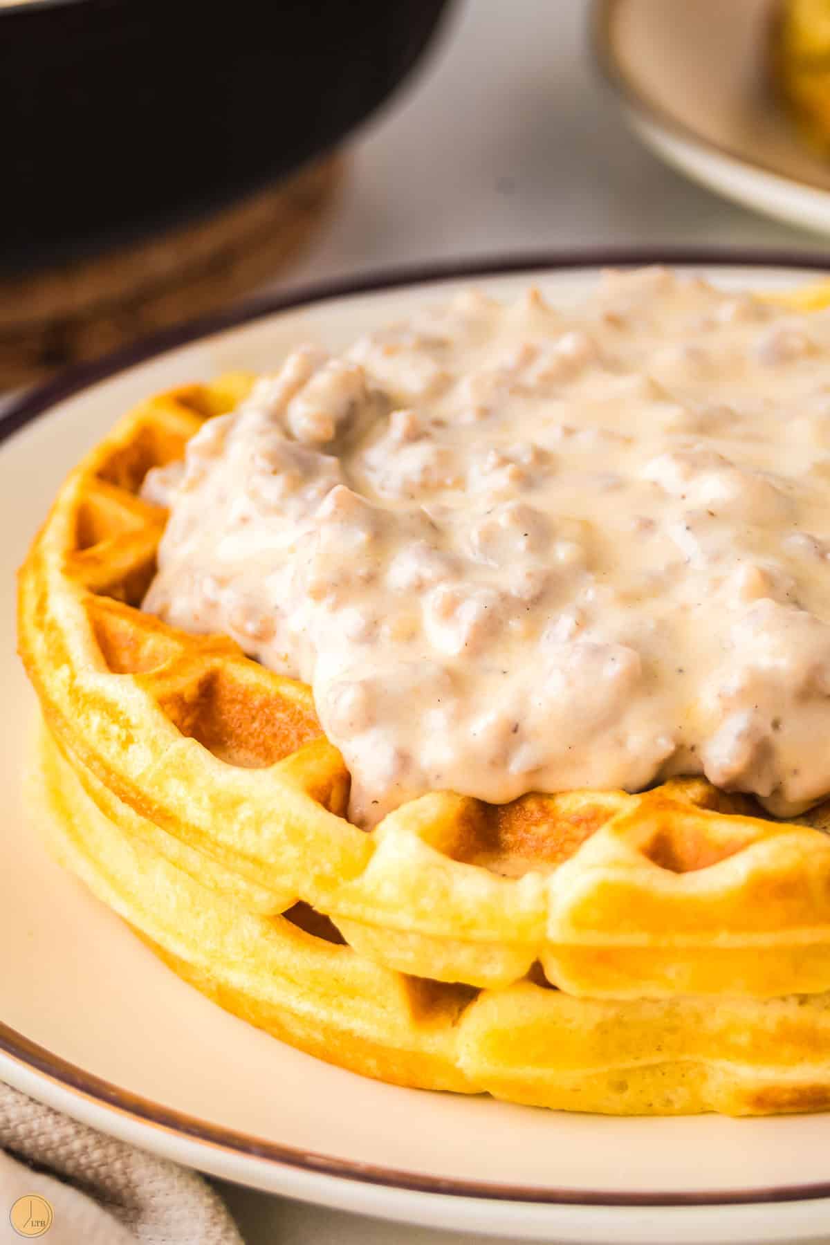 close up of side of stack of waffles with pork sausage gravy on them