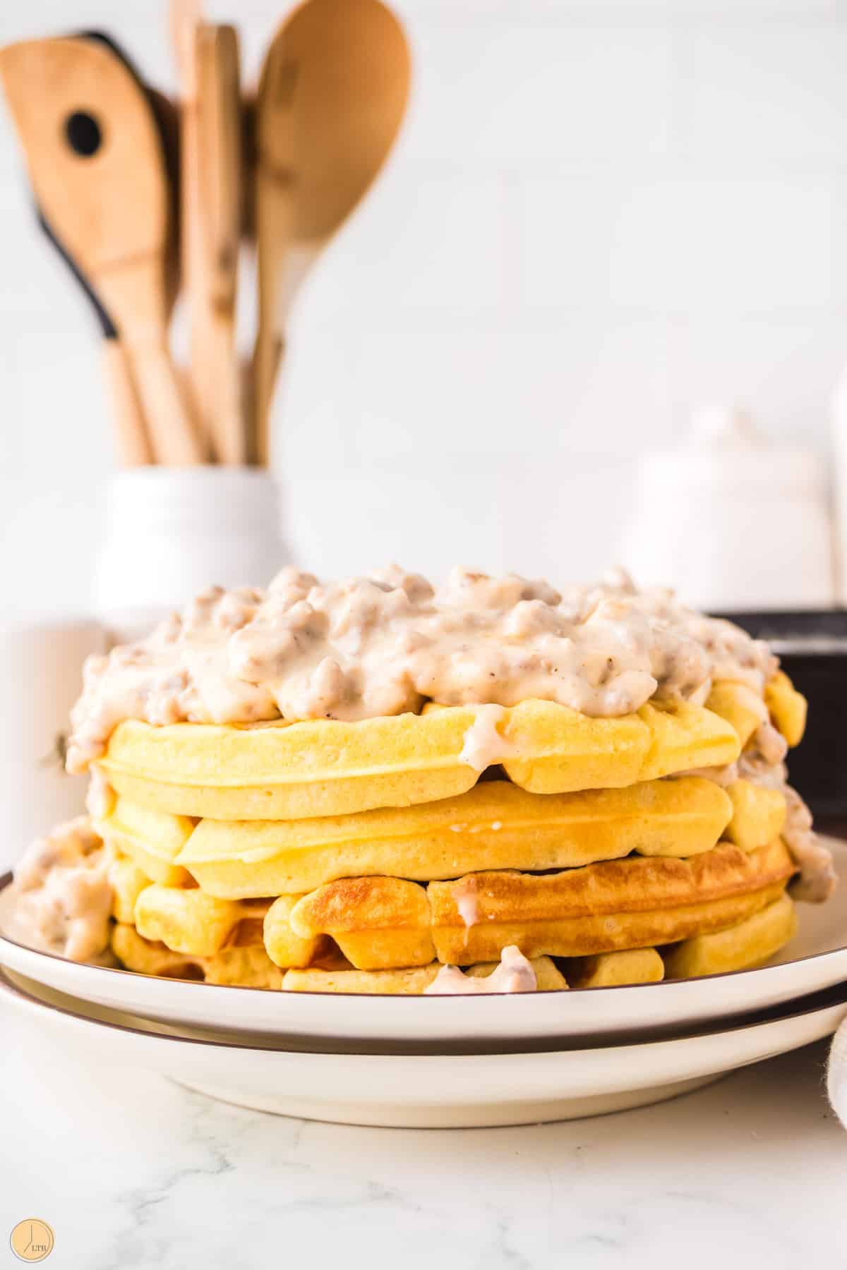stack of three waffles covered in sausage gravy with a jar of wooden spoons behind it