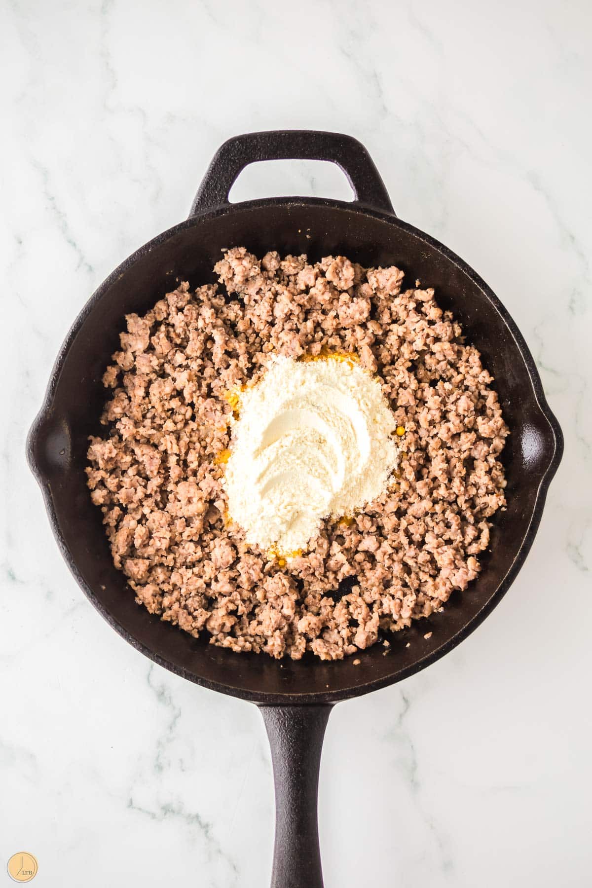 cooked pork sausage in a cast iron skillet with flour sprinkled in the center