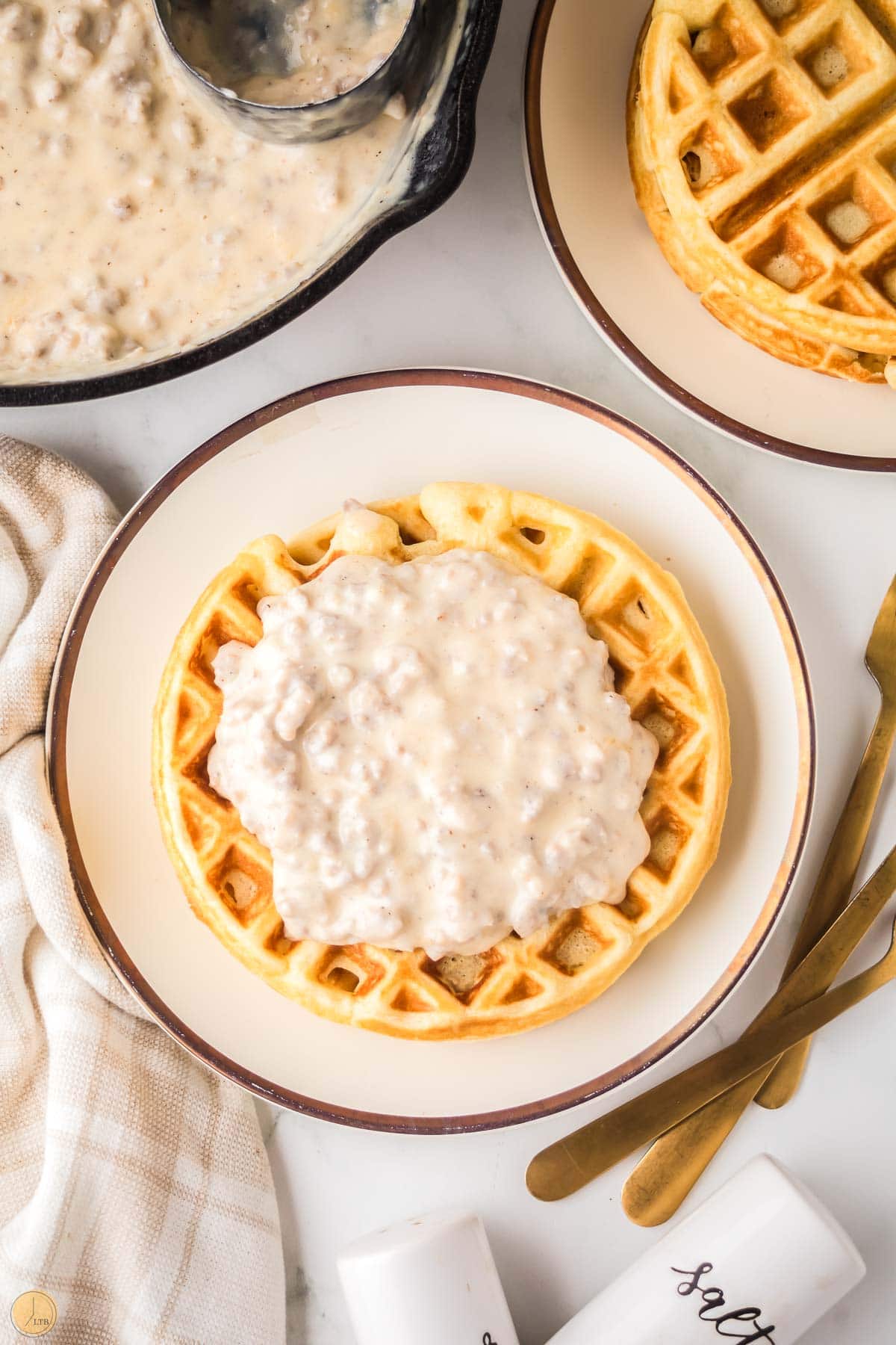 white plate with a waffle on it topped with sausage gravy